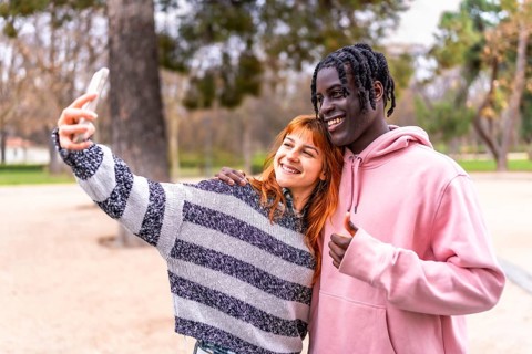 Happy multi ethnic couple enjoying a sunny day in the park, taking a cheerful selfie while flashing