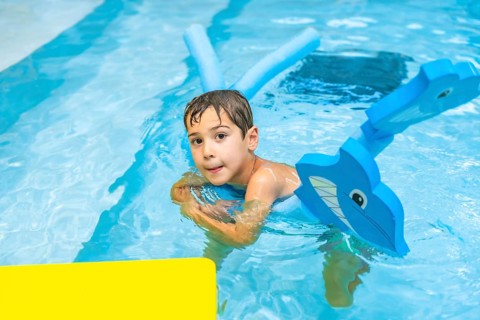 Happy boy playing with inflatable toy whale in swimming pool during summer vacation, enjoying