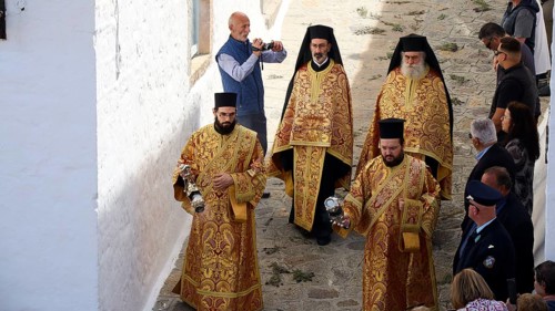 Clerics in richly decorated robes walk along a stone alley, spectators take photos, Orthodox