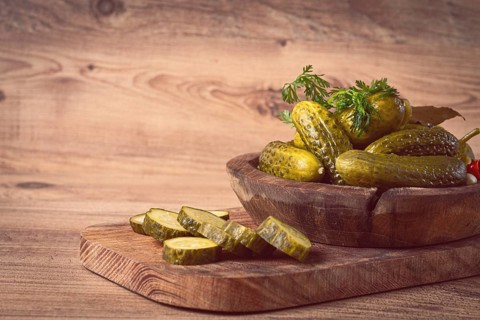 Pickled cucumbers in a wooden bowl with herbs and spices, close-up, rustic style