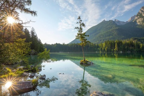 Sun star at sunrise at Hintersee near Ramsau in Berchtesgadener Land with sun star and reflection.