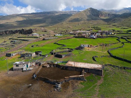 Small village surrounded by green meadows and mountains, clear sky with clouds in the background,