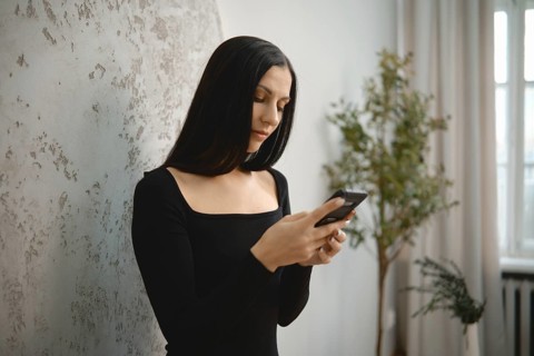 Woman with long black hair using smartphone in a minimalist indoor space during the day