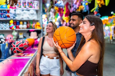 Group of friends enjoying a lively evening at a funfair game stall, celebrating their basketball