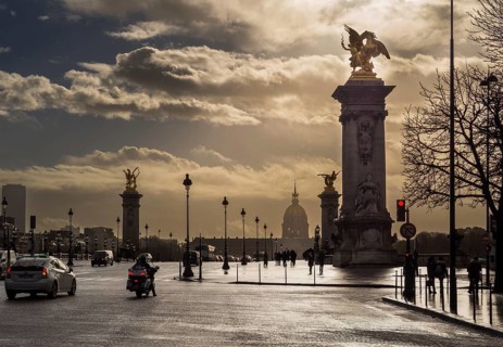 Clouds gather above the iconic Alexandre III Bridge as vehicles and people navigate the bustling