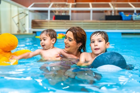 Smiling mother enjoying time with her sons while swimming in an indoor pool, playing joyfully with