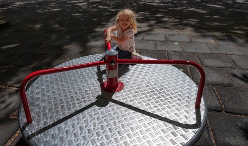 Outdoor shot, little girl, 3 years old, blonde, playing on a merry-go-round, children's playground,