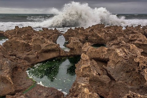 A rocky area with a hole in the ground. The hole is filled with water. The water is brown in colour