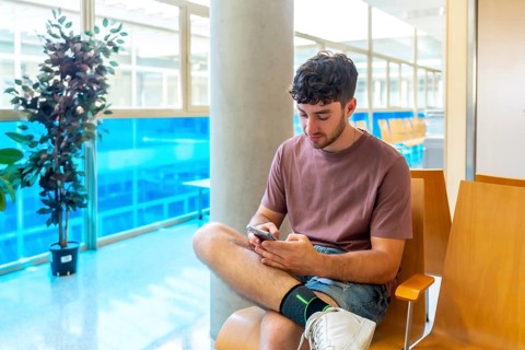 Patient sitting comfortably in a bright waiting room, using a smartphone to stay connected and