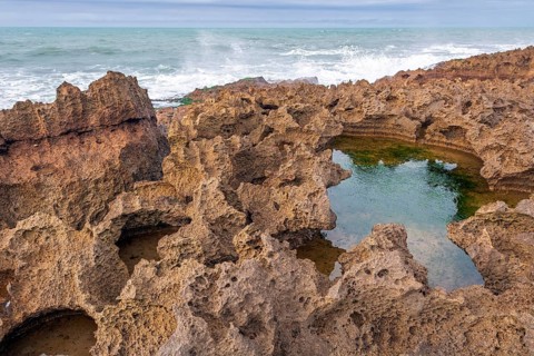A rocky area with a hole in the ground. The hole is filled with water. The water is brown in colour