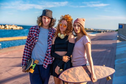 Three friends with skateboards relax by the seaside, enjoying the sunny weather and casual outdoor