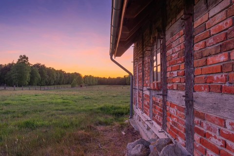 View along an outer wall of a half-timbered barn standing on a pasture in the sunset, meadow,