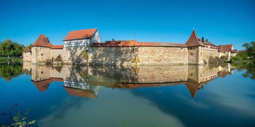 The town wall with defence towers and half-timbered house is reflected in the lake pond,