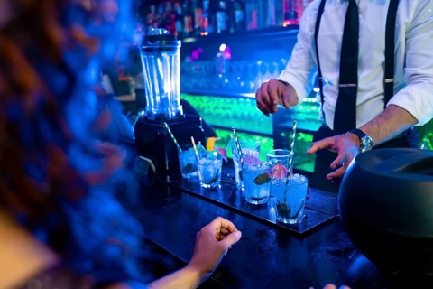 Bartender skillfully preparing vibrant blue cocktails garnished with fresh mint and ice in a lively