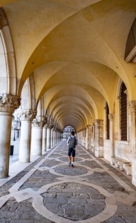 Young man walking through the portico of the Doge's Palace, St Mark's Square, Venice, Veneto, Italy
