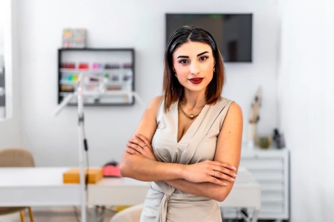 Young female entrepreneur posing with crossed arms in her hair and beauty salon, looking confident