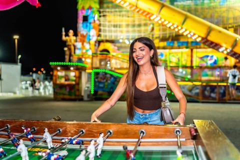 Happy young woman enjoying a vibrant evening at a funfair, playing table football and soaking up