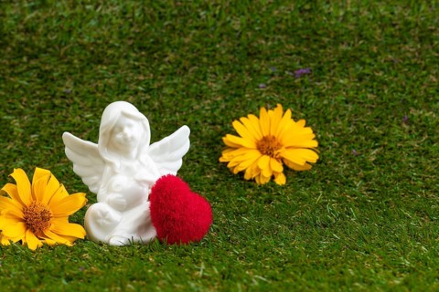An angel figure with a red heart and yellow flowers on green grass
