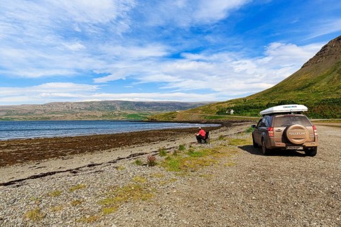 Tourist enjoying solitude in fjord landscape, SUV with roof tent, Skápadalur valley, coastline,