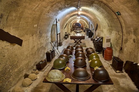 A tunnel with a row of helmets on a table, in the background exhibits, steel helmets, war museum,