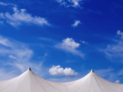 Exhibition tent under a bright blue sky adorned with fluffy clouds in a lively outdoor setting