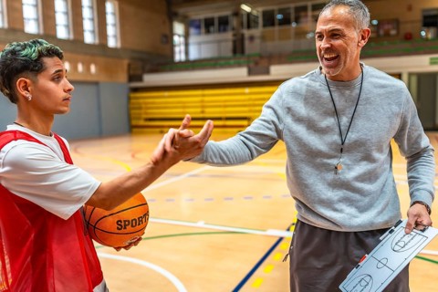Basketball coach explaining game strategy using clipboard to young player holding ball in a