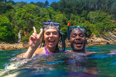 Young multi ethnic couple enjoying snorkeling together in crystal clear tropical sea, woman making