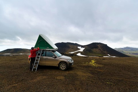 Barren volcanic landscape with snowfields, off-road vehicle with roof tent and ladder on mountain