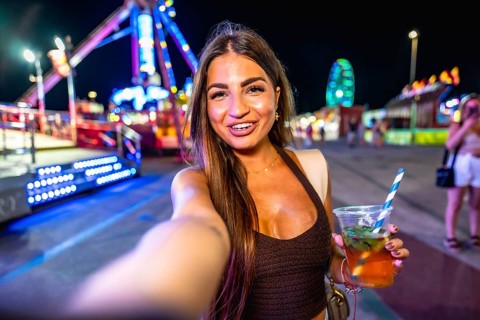 Happy young woman enjoying a vibrant night at an amusement park, taking a selfie while holding a