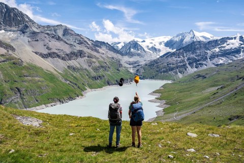 Two female friends throw their hats in the air, female mountaineers in front of a blue mountain