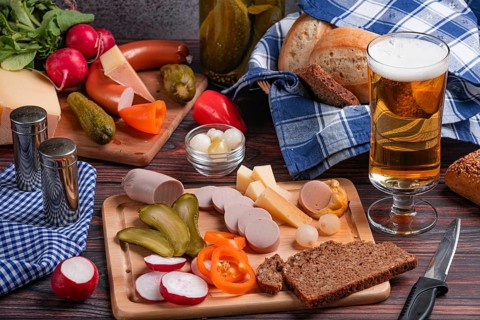 Rustic snack with sausage, cheese, beer, mustard, vegetables and bread on a laid table
