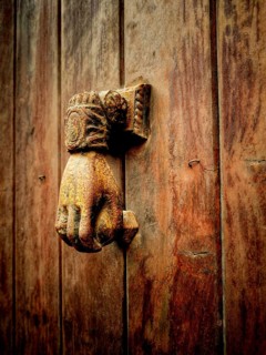 A vintage hand-shaped door knocker is mounted on a weathered wooden door, showcasing intricate