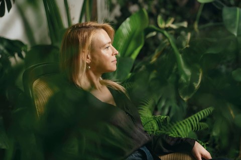 A woman sits quietly in a cozy chair within a vibrant indoor garden filled with lush plants and