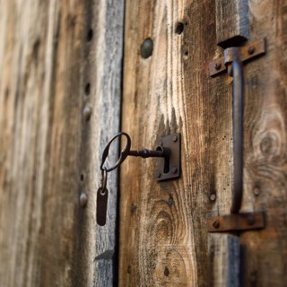 Close-up view of a rustic wooden door featuring a vintage lock and key. The texture of the wood and