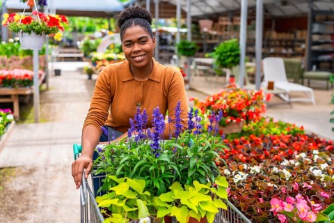 Smiling afro american woman pushing a shopping cart filled with vibrant flowers while browsing in a