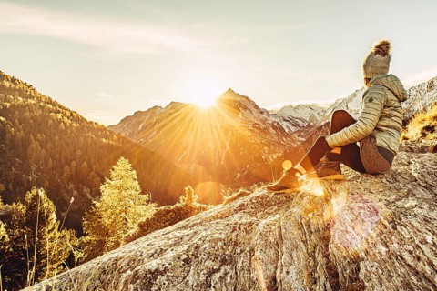 Woman sitting thoughtfully at a feslen at autumn atmosphere during sunset in the Swiss Alps in the