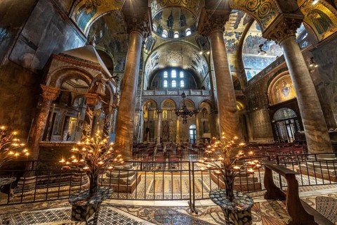 Lit candelabras illuminate the mosaic decorations and marble columns inside saint mark's basilica