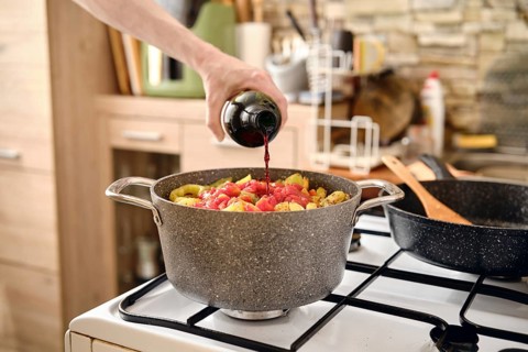 A person pours red wine into a pot filled with pork and vegetables making aromatic sauce