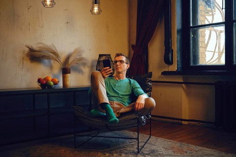 A middle-aged man sits in a chair and looks at the smartphone screen. He made an online order and
