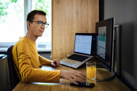 A man in a yellow shirt sits at a desk in a home office. He was distracted from studying statistics