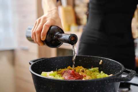 A hand pours liquid into a pot filled with chopped vegetables and sauce, creating a delicious