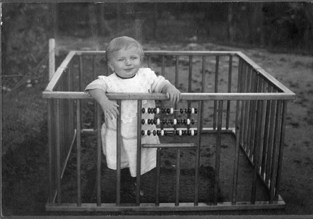 Child in a playpen, 1920s, A smiling child stands in a grid with an abacus in a nostalgic,