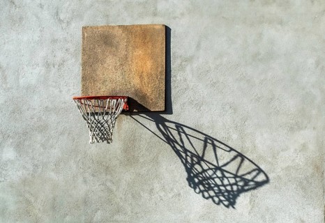 A worn basketball hoop is mounted on a textured wall, with the sunlight creating a captivating