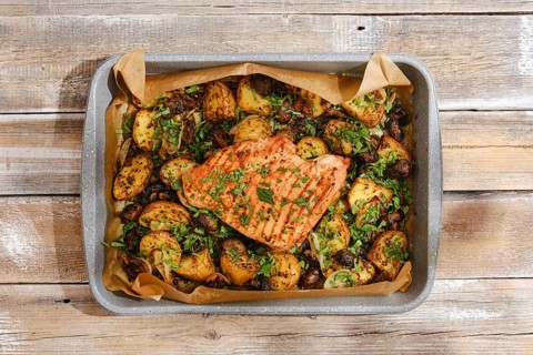 A roasted turkey breast rests atop a bed of golden, seasoned potatoes, vibrant herbs sprinkled over