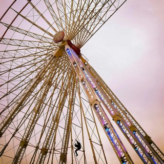 A maintenance worker is seen climbing the structure of a ferris wheel that features vibrant lights.
