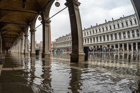 Tourists visiting piazza san marco in venice, italy, despite the rain causing flooding under the