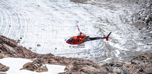 Red helicopter flies over glaciers in the mountains, Stubai Alps, South Tyrol, Italy