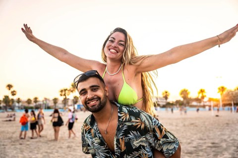 Carefree woman enjoying piggyback ride on man's back, spreading arms wide with joy on a sunny beach