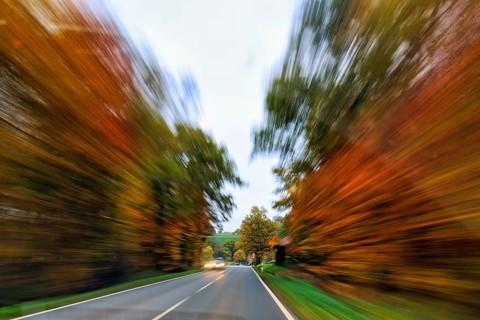 Country road through autumn forest, autumn leaves, oncoming traffic, light traces, cloudy weather,