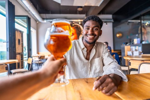 Waiter serving a refreshing glass of beer to a smiling young man in a stylish modern pub, creating